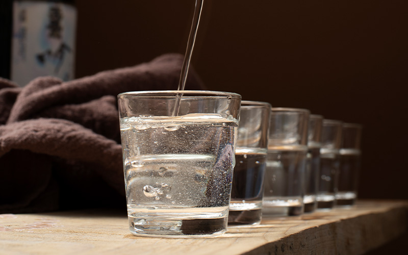 clear-baijiu-spirit-being-poured-into-small-tasting-glasses-lined-up-on-wooden-table