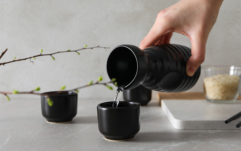 Pouring traditional Japanese sake into small black ceramic cup.