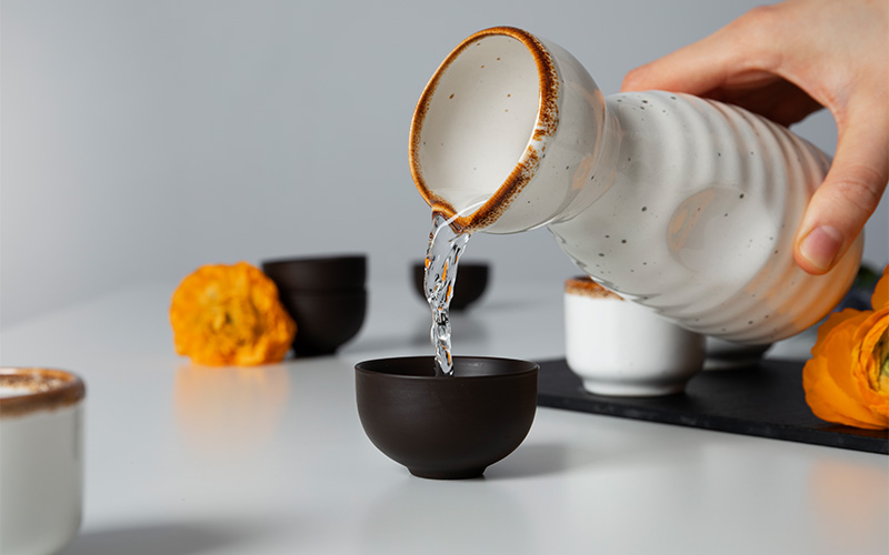 Pouring Japanese sake from a ceramic carafe into a cup